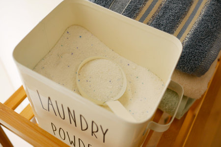 Laundry powder container with scoop and towels nearby