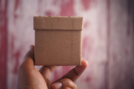 Hand holding a small brown box against a textured background