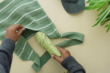 Preparing a green tote bag with an umbrella and cap indoorsの写真素材