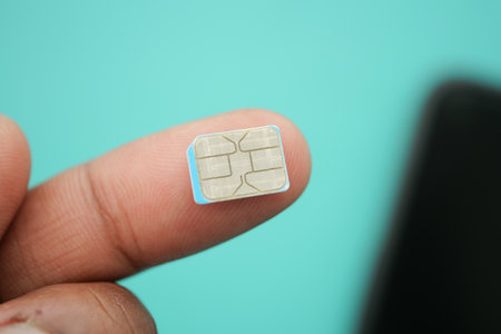 Tiny SIM card held between fingers against blue backgroundの写真素材