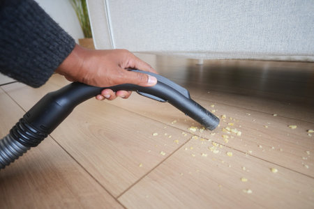 Vacuuming crumbs from wooden floor with attention to detailの写真素材