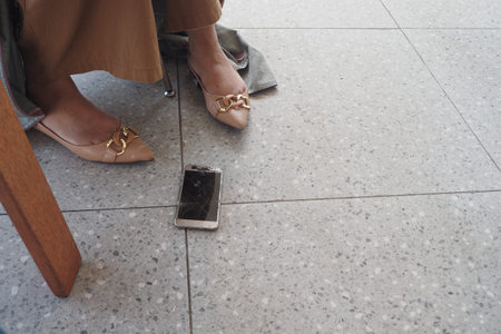 Woman in heels sits near cracked smartphone on floor