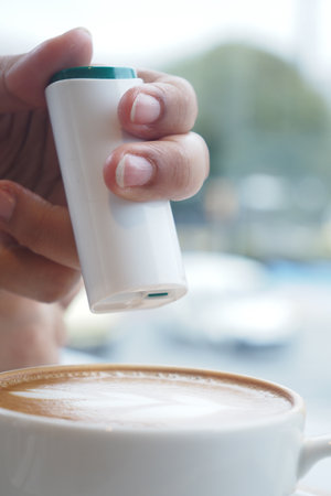 Hand holding artificial sweetener container above coffee cup.の写真素材