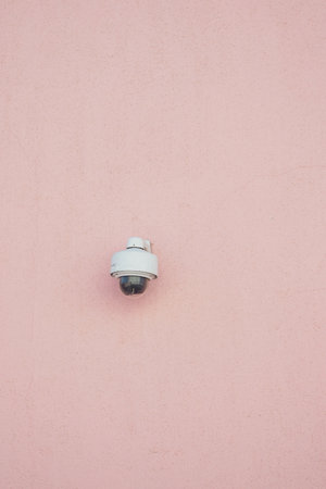 Security camera mounted on a pink wall in bright daylightの写真素材