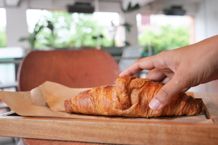 Hand reaching for a freshly baked croissant on a wooden trayの写真素材