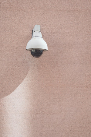 Security camera mounted on a textured pink wallの写真素材