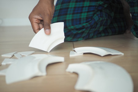 Person carefully handling broken ceramic pieces on the floorの写真素材