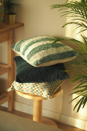 Decorative cushions stacked on a wooden stool in sunlight