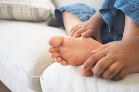 A young child is sitting on a couch, rubbing their bare foot contentedlyの写真素材