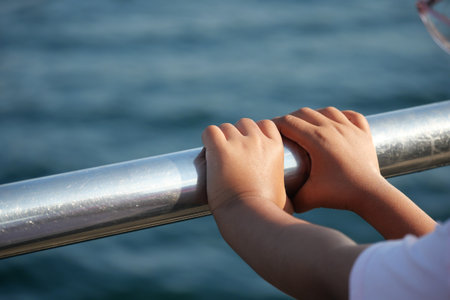 Childs hands gripping metal railing by the waterの写真素材