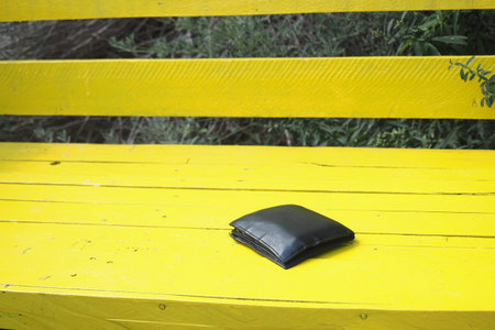 Wallet resting on a bright yellow park bench. lost wallet concept