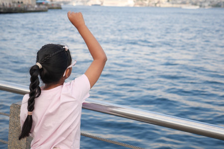 Child waving joyfully at the waterfront on a sunny dayの写真素材