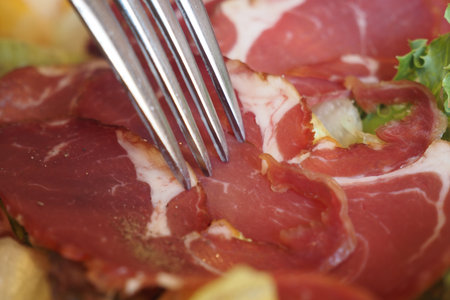 Close-Up of Fork on Italian Cured Meat with Crisp Lettuceの写真素材