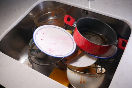Dishes piled high in a kitchen sink after a busy mealの写真素材