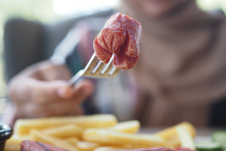 Juicy meat on fork beside golden fries at a dining tableの写真素材