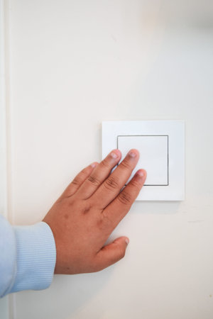 Child Hand pressing a light switch on a white wall