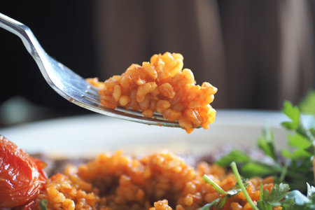 Delicious forkful of bulgur rice and vegetables at a dining tableの写真素材