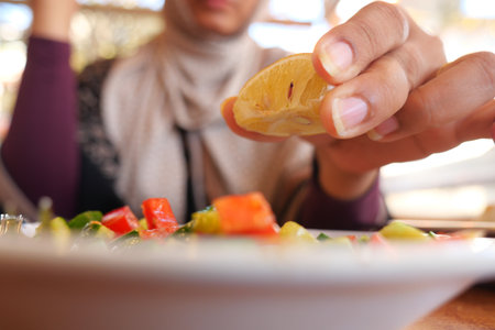 A person squeezes fresh lemon juice onto a vibrant salad during lunchの写真素材