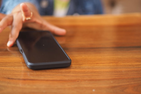 Child hand reaching for smartphone on wooden table surface