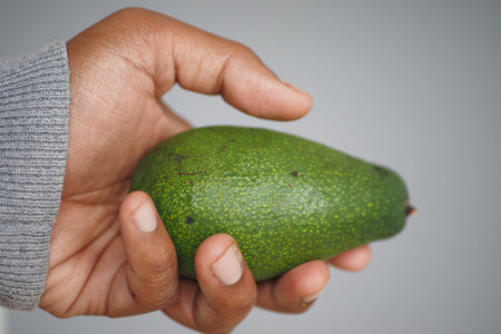 Holding a ripe green avocado in a hand