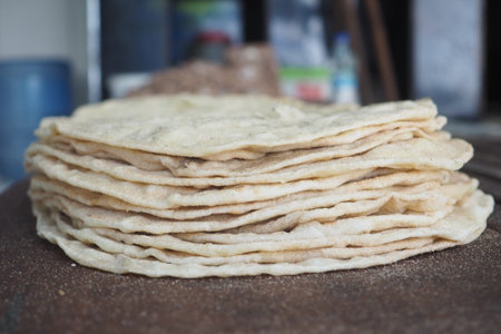 Homemade flatbreads stacked on wooden surface in kitchenの写真素材