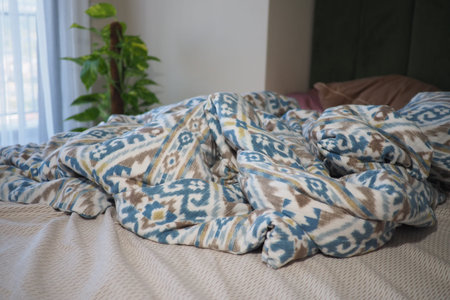 Cozy blanket draped on a bed in morning lightの写真素材