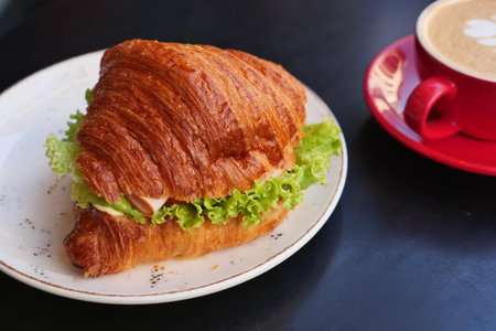 Fresh croissant sandwich with coffee in a cafe settingの写真素材