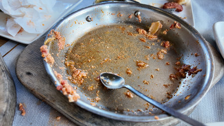 Leftover food in metal dish after meal at restaurant