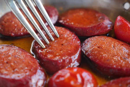Sliced sausage cooked in oil with fresh peppers on a plateの写真素材