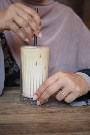 Hand holding iced drink at cafe table in afternoon light
