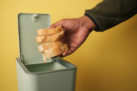 Hand disposing of stale bread in a green trash canの写真素材