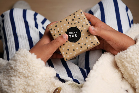 A child holds a small gift box while sitting on a comfortable surfaceの写真素材