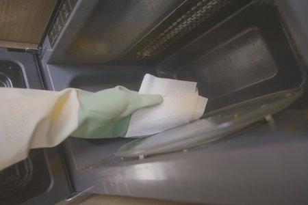 Cleaning a microwave with paper towels in a kitchenの写真素材