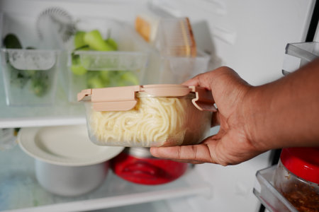 Hand holding a container of spaghetti from a fridgeの写真素材