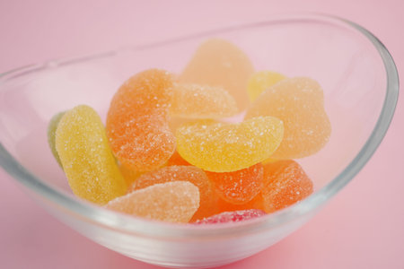 Colorful gummy candies in a clear bowl on a pink surface