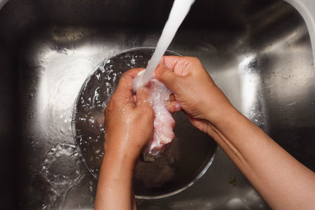 Washing chicken in a clear bowl under running waterの写真素材