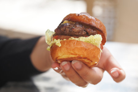 Delicious homemade burger held by a hand outdoorsの写真素材