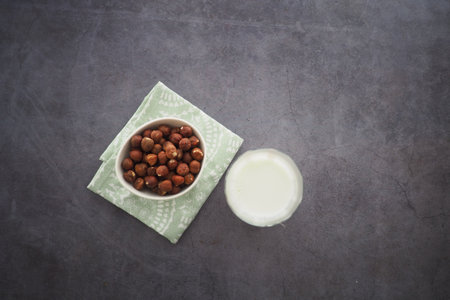 Bowl of hazelnuts and a glass of milk on a textured surfaceの写真素材