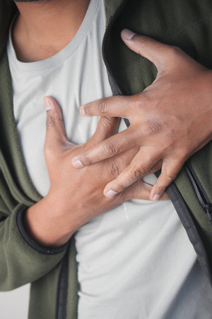 Man experiences chest pain while holding his heartの写真素材