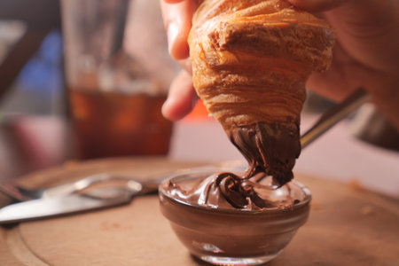 Enjoying a croissant dipped in chocolate sauce at a cafeの写真素材