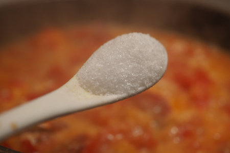 Adding salt to a sauce to balance flavor during cookingの写真素材