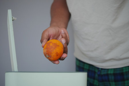 Disposing of a rotting orange in a trash binの写真素材