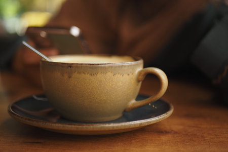 Warm coffee cup on a wooden table near a smartphoneの写真素材