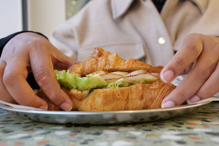 Enjoying a delicious croissant sandwich at a cafeの写真素材
