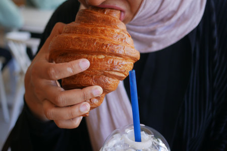 Enjoying a croissant and drink at a cozy cafeの写真素材