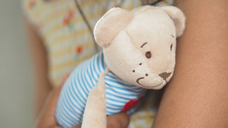 Child holds a soft toy bear while sitting quietlyの写真素材
