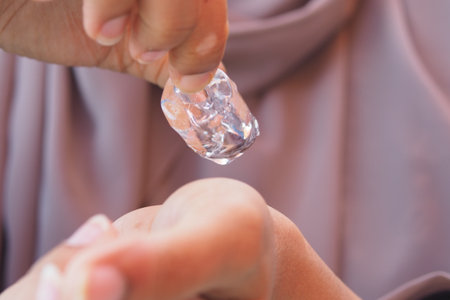 Hand holding ice cube over skin for cooling effectの写真素材