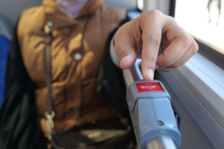 Hand presses stop button on bus during a ride