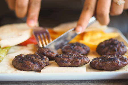 Grilling meat patties with a fork and knife at a table