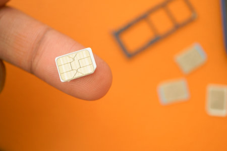 SIM card held by a finger on an orange backgroundの写真素材
